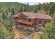 Expansive aerial view of a brown house surrounded by lush greenery, showcasing its spacious deck and scenic setting at 7790 S Homesteader Dr, Morrison, CO 80465