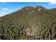 An aerial view captures a charming mountain home surrounded by a dense forest on a sunny day at 4560 Hilltop Rd, Evergreen, CO 80439