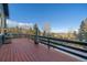 Spacious wooden deck with black railing, featuring a rustic outdoor fireplace and scenic wooded views at 11222 Conifer Mountain Rd, Conifer, CO 80433