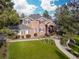 View of the red brick two-story home with gray roof and mature trees around the green grass yard at 5428 Golden Currant Way, Parker, CO 80134