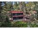 Charming mountain cabin with a red roof, surrounded by lush greenery and mature trees at 5672 Santa Clara Rd, Indian Hills, CO 80454