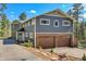 Two-story home with a stone-clad garage and gray siding, surrounded by trees and a blue sky at 4574 Picutis Rd, Indian Hills, CO 80454