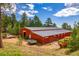Exterior view of a red barn with a metal roof surrounded by trees, equipment and truck at 8838 Hillview Rd, Morrison, CO 80465