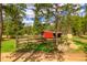 This small red barn and fenced-in area are surrounded by towering green trees on a sunny day at 8838 Hillview Rd, Morrison, CO 80465
