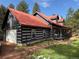 Beautiful cabin with red metal roof, white-trimmed windows, and attached garage, nestled among tall pine trees at 9716 Canon Dr, Sedalia, CO 80135