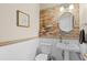 A stylish half-bathroom with a brick accent wall, pedestal sink, and decorative mirror that is well-lit at 13723 Milwaukee Ct, Thornton, CO 80602