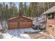 Two-car garage featuring rustic design and surrounded by snow-covered landscapes and mature trees at 266 Lodgepole Dr, Evergreen, CO 80439