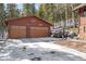 Two-car garage featuring rustic design and surrounded by snow-covered landscapes and mature trees at 266 Lodgepole Dr, Evergreen, CO 80439