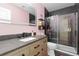 Modern bathroom with pink walls, black tile, frameless glass shower and a light wood vanity with gray counters at 17851 Herrera Dr, Parker, CO 80134