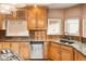 A kitchen with wood cabinets, tiled backsplash, stainless steel dishwasher, and sink by a window at 3231 Oak St, Wheat Ridge, CO 80033