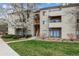 Charming condo building with multiple units, balconies, and shared outdoor space featuring vibrant green grass and mature tree at 7468 S Alkire St # 204, Littleton, CO 80127