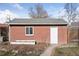 A brick building featuring a white door, window, and landscaped garden bed under a gray roof at 1580 Quince St, Denver, CO 80220