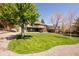 Large, meticulously mowed backyard with green grass, a two-story deck, mature trees, and a gravel perimeter at 6668 Fairways Dr, Longmont, CO 80503