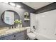 Stylish bathroom with granite countertop, round mirror, dark gray wall, and shower-tub combo at 6167 S Pierson St, Littleton, CO 80127