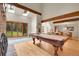 Spacious living room with a pool table, fireplace, wood beams, skylights and a large window showcasing the outdoor scenery at 8851 Blue Creek Rd, Evergreen, CO 80439
