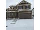Two-story home featuring a covered porch, two-car garage, and steps leading to the front door, with snow covering the yard at 4995 S Algonquian Way, Aurora, CO 80016
