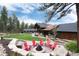 Landscaped backyard with a fire pit, seating, lush green lawn, and a beautiful home with views of towering trees at 44 N Big Meadow Trl, Franktown, CO 80116