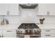 Close-up of stainless steel gas range in a bright kitchen with white cabinets and tiled backsplash at 3011 W 53Rd Ave, Denver, CO 80221