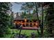Well-lit exterior showing a wall of windows and a wooden deck with seating area surrounded by mature trees at 25257 Snyder Ave, Conifer, CO 80433