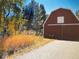 Rustic red barn with a metal roof, surrounded by autumn foliage and a paved driveway at 27436 Kennedy Gulch Rd, Conifer, CO 80433