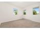 This bedroom has bright white walls, neutral carpet, and two windows overlooking the lush outdoors at 14475 Lanewood St, Brighton, CO 80603