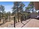 Expansive deck with metal railing offers serene views of the surrounding landscape and mature trees at 31607 Broadmoor Dr, Evergreen, CO 80439