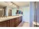 Bright bathroom with double sinks, wood cabinets, large mirrors, and shower with glass door at 8233 E 149Th Dr, Thornton, CO 80602