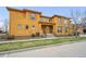 Two-story yellow townhouse featuring a well-maintained lawn, concrete steps, and street parking at 7777 E 23Rd Ave # 203, Denver, CO 80238
