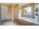 Relaxing bathroom with a tiled soaking tub, window, and tiled floors, complemented by neutral-toned walls at 2882 Signal Creek Dr, Thornton, CO 80241
