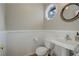 A half bathroom features a sink, toilet, wall paneling, and stylish octagonal mirror and window at 7835 Nelson St, Arvada, CO 80005