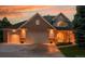 Charming brick home with a three-car garage illuminated by warm exterior lights and a beautiful sunset at 7472 S Utica St, Littleton, CO 80128