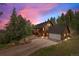 Exterior view of a brown home with a gray roof and attached garage surrounded by lush trees under a vibrant sunset sky at 32462 Lodgepole Dr, Evergreen, CO 80439