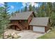 Exterior shot of a brown two-story home with a gray roof and attached garage surrounded by lush trees and a stone landscape at 32462 Lodgepole Dr, Evergreen, CO 80439