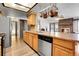 Open kitchen with wood cabinets, stainless steel dishwasher, and a view into the adjacent living room with a brick fireplace at 10142 Josephine St, Thornton, CO 80229