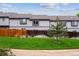 View of townhomes with gray siding, surrounded by green grass, and a wooden fence at 1953 E 102Nd Cir, Thornton, CO 80229