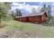 Exterior view of a cozy, rustic home featuring warm wood siding, surrounded by a lush, green lawn and mature trees at 26367 Pressler St, Conifer, CO 80433