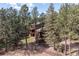Aerial view of a home surrounded by tall pines, with decks, fenced yard, and barn at 133 Mine Ln, Boulder, CO 80302