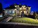 Elegant stone home at night with exterior lighting and a well-manicured lawn and landscaped front yard at 10704 Flowerburst Ct, Highlands Ranch, CO 80126