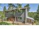 View of the two-story house exterior surrounded by greenery, a wooden deck, and a small greenhouse on the side at 30273 Conifer Rd, Evergreen, CO 80439