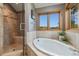 Bathroom showcasing soaking tub, window with tree view, and tiled shower with glass door at 30444 Ruby Ranch Rd, Evergreen, CO 80439