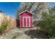 Red storage shed in backyard with wood fence, plants, and a mature flowering tree at 8325 Elati St, Denver, CO 80221
