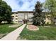 Inviting condo complex featuring a manicured lawn, mature trees, and charming architectural details at 9155 E Center Ave # 4B, Denver, CO 80247