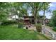 Spacious backyard featuring a stone patio with outdoor seating, a fire pit, mature trees, and lush greenery at 1415 S Jasmine Way, Denver, CO 80224