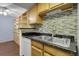 Kitchen sink with wood cabinets, black countertop and tile backsplash at 8225 Fairmount Dr # 102, Denver, CO 80247