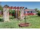 Charming front yard featuring a decorative pergola, red fence, picnic table and vibrant green lawn at 2401 W Jewell Ave, Denver, CO 80219