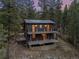 Two-story home with wooden balconies and a brick patio at dusk surrounded by lush trees and greenery at 27891 Columbine Rd, Evergreen, CO 80439