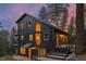 Two-story home featuring a black facade, multi-level deck, and surrounded by mature trees at sunset at 27891 Columbine Rd, Evergreen, CO 80439