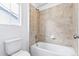 Bathroom featuring a tiled shower over tub with neutral-toned wall tiles and a toilet next to a small window at 3315 N Coolidge Way, Aurora, CO 80019