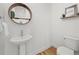Cozy half bathroom with a pedestal sink, round mirror, and a modern toilet at 21440 E 61St Dr, Aurora, CO 80019