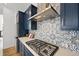 Close-up of a gas stovetop, stainless steel vent hood, and intricate tile backsplash in the modern kitchen at 21440 E 61St Dr, Aurora, CO 80019